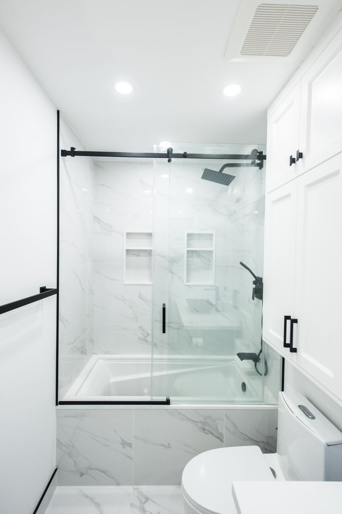Sleek and modern bathroom featuring white marble tiles, glass shower doors, and black accents.